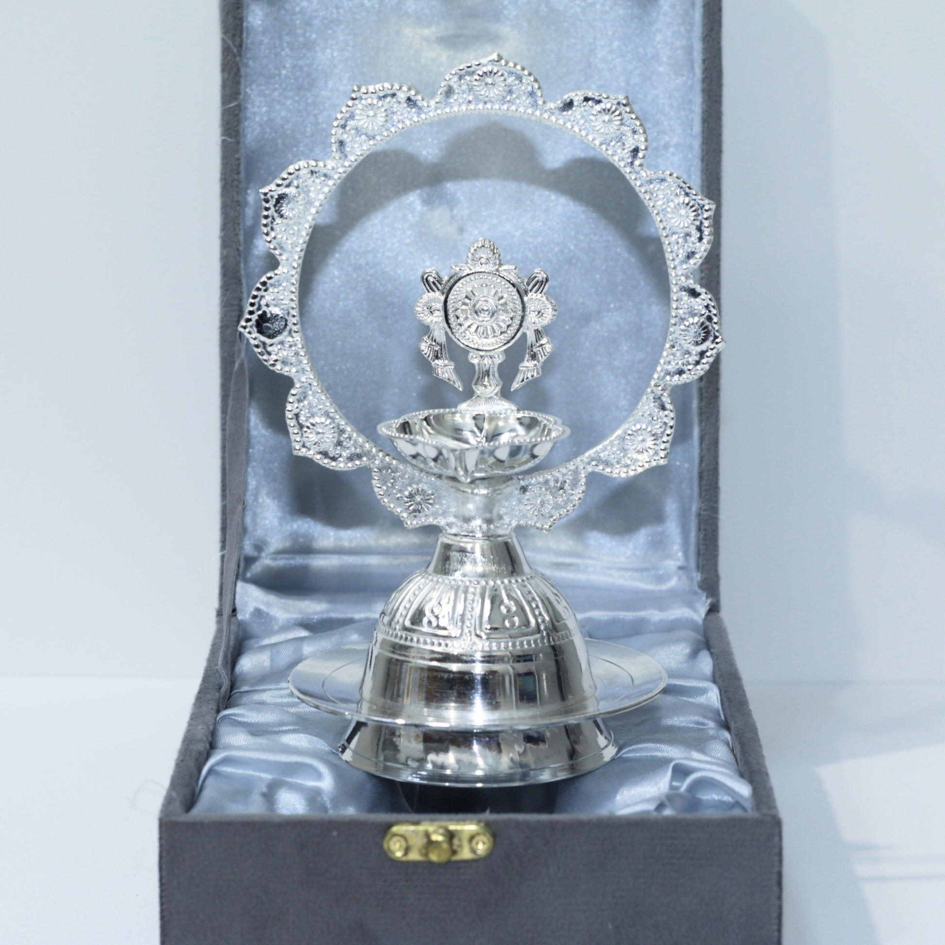 Silver deepak with intricate design in a box on a light gray background