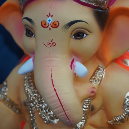 A close-up of a Lord Ganesha idol with a pink turban, silver ornaments, and a beige face and trunk, shown against a dark background.