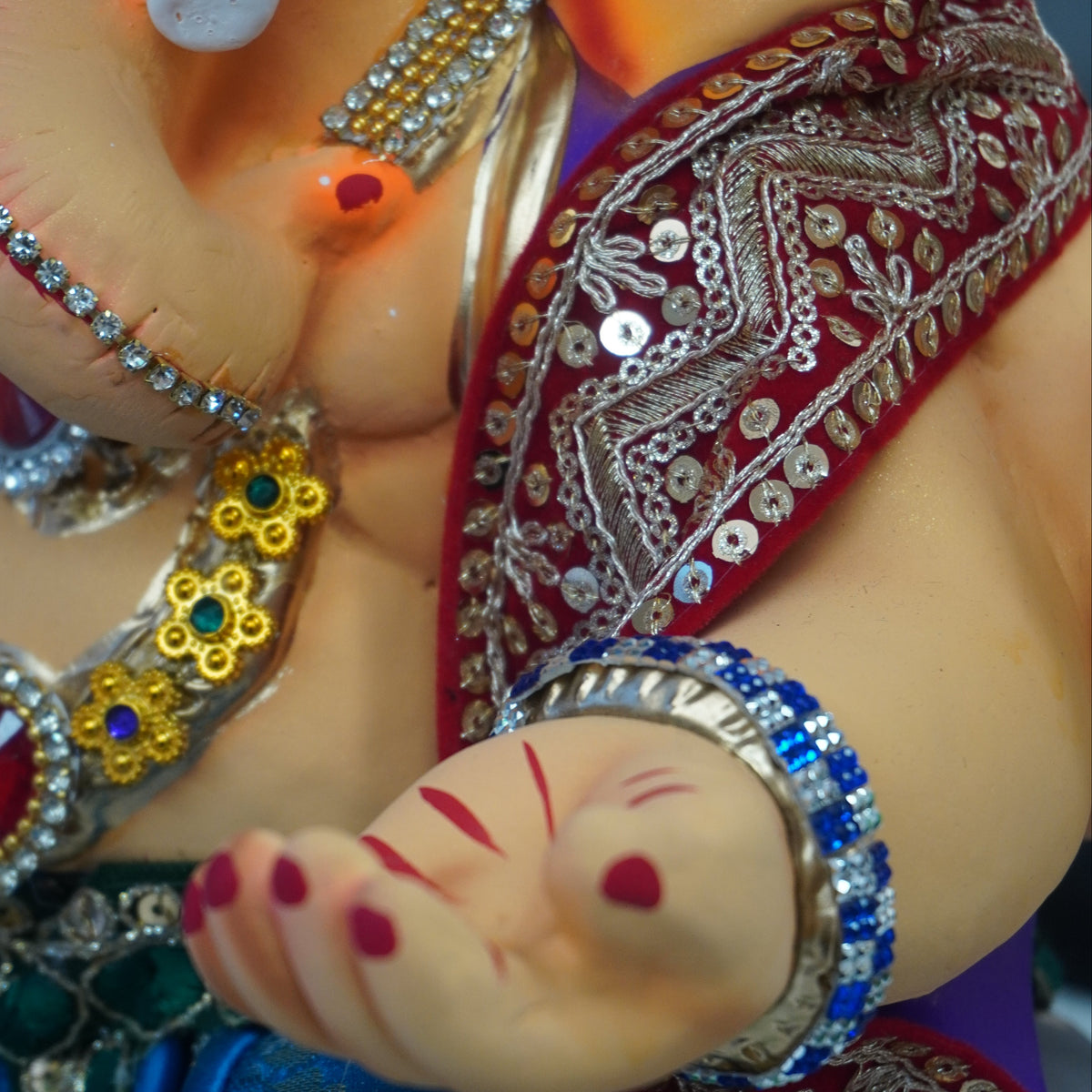 Close-up of a decorated Ganesha idol, showing the elephant trunk, jeweled necklace, red sash, blue fabric, and painted hand with red markings.