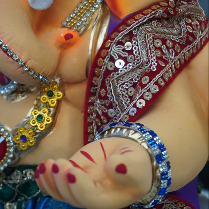 Close-up of a decorated Ganesha idol, showing the elephant trunk, jeweled necklace, red sash, blue fabric, and painted hand with red markings.