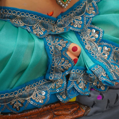 Close-up of a turquoise blue embroidered garment with silver mirror-work borders, a jeweled necklace, and a small peek of a person's hand with red nail polish.