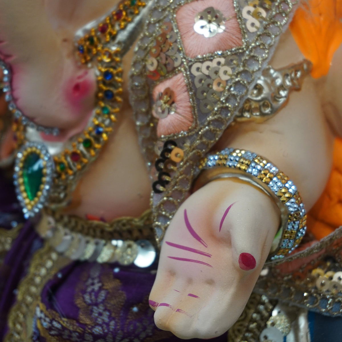 Close-up of a decorated Hindu deity idol, showing the hand with the Golu (fingers) and ornate gold and pink embellished clothing.