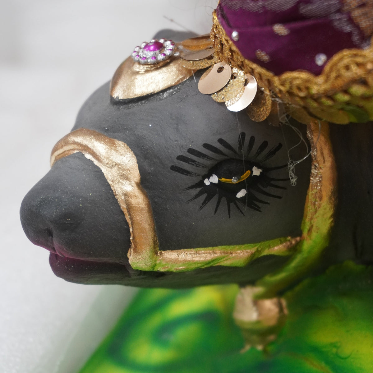 A close-up of a hand-painted folk art figurine depicting a horse adorned with gold-colored trim, a purple crown, and a vibrant green patterned base.