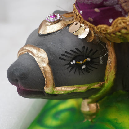 A close-up of a hand-painted folk art figurine depicting a horse adorned with gold-colored trim, a purple crown, and a vibrant green patterned base.